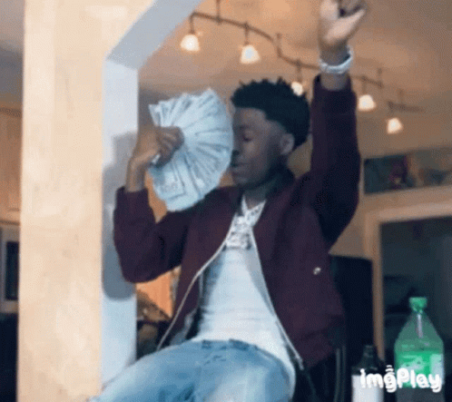 A Man In A Maroon Jacket Is Holding A Fan Of Money In His Hands . GIF