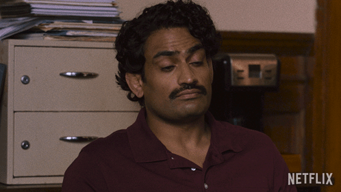 A Man In A Maroon Shirt Is Sitting In Front Of A Netflix Logo GIF