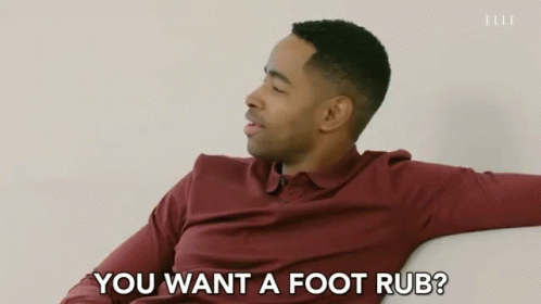 A Man In A Maroon Shirt Is Sitting On A Couch And Says " You Want A Foot Rub " GIF