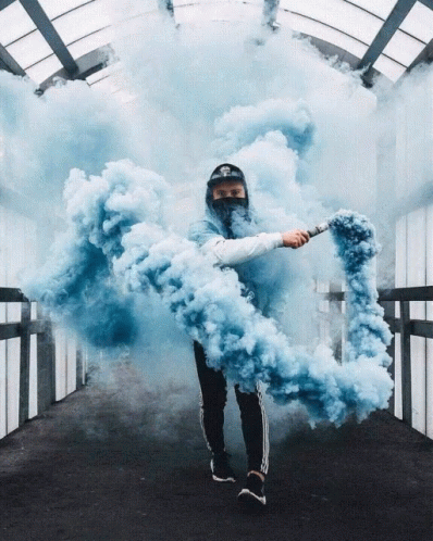 A Man In A Mask Holds A Blue Smoke Bomb In His Hand GIF