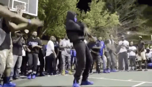 A Man In A Mask Is Dancing On A Basketball Court In Front Of A Crowd Of People . GIF