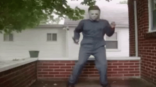 A Man In A Mask Is Dancing On A Porch In Front Of A Brick House . GIF
