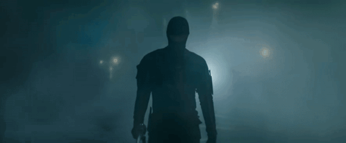 A Man In A Mask Is Holding A Gun In A Dark Room . GIF