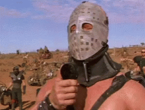 A Man In A Mask Is Holding A Microphone In A Desert . GIF