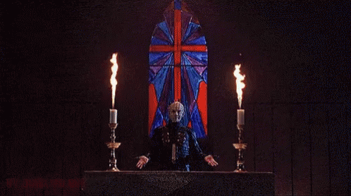 a man in a mask is holding two candles in front of a burning building .