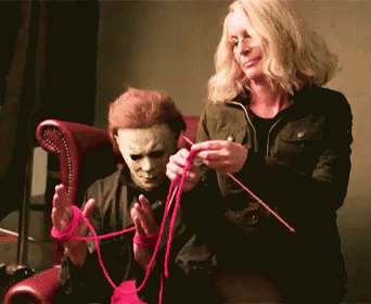A Man In A Mask Is Sitting Next To A Woman Who Is Knitting GIF
