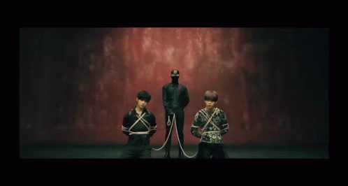 A Man In A Mask Is Standing Behind Two Men Tied Up With Ropes GIF