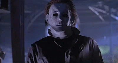 a man in a mask is standing in a dark room and looking at the camera .