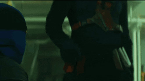 A Man In A Mask Is Standing In A Dark Room With The Word Poser Written Above Him GIF