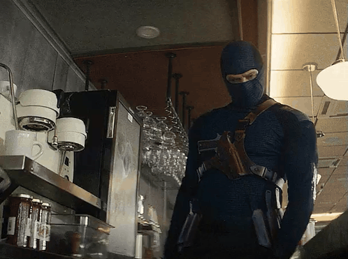 A Man In A Mask Is Standing In Front Of A Coffee Machine GIF
