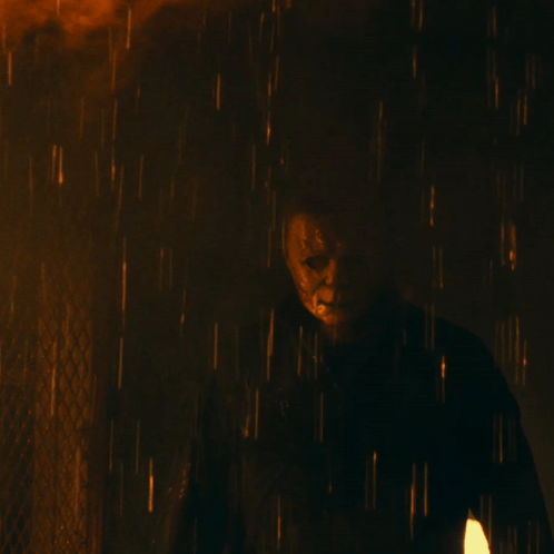 a man in a mask is standing in the rain with a fire in the background