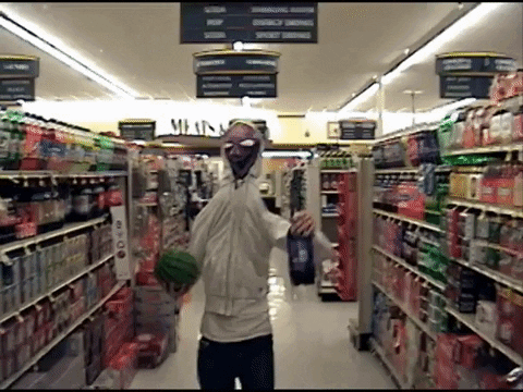 A Man In A Mask Is Walking Through A Grocery Store Aisle With A Sign That Says Meats GIF