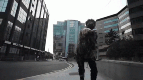 A Man In A Mask Walks Down A Street In Front Of A Building GIF
