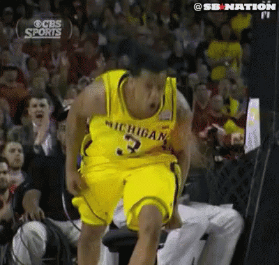 A Man In A Michigan Jersey Is Jumping In The Air In Front Of A Crowd GIF