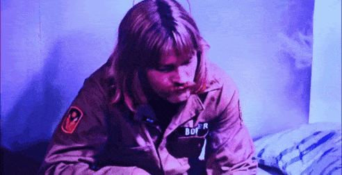 a man in a military jacket with the word bof on his chest is sitting on a bed .