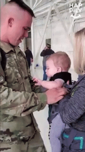 A Man In A Military Uniform Holds A Baby In A Carrier GIF