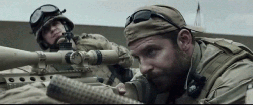A Man In A Military Uniform Is Aiming A Sniper Rifle . GIF