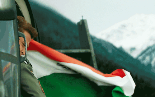 A Man In A Military Uniform Is Holding A Flag In Front Of A Mountain GIF