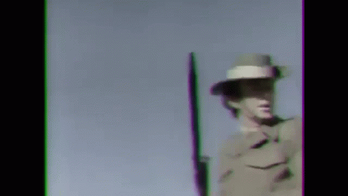 A Man In A Military Uniform Is Holding A Rifle Against A Blue Sky . GIF