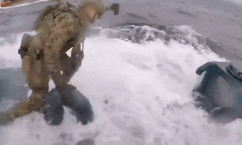 A Man In A Military Uniform Is Kneeling In The Water . GIF