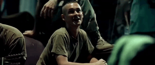 A Man In A Military Uniform Is Laughing While Sitting On The Ground . GIF