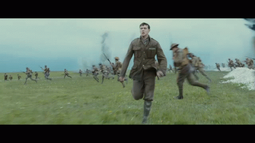 A Man In A Military Uniform Is Running In A Field With Soldiers Behind Him GIF