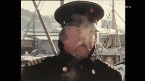 A Man In A Military Uniform Is Smoking A Cigarette While Wearing A Hat With A Star On It . GIF