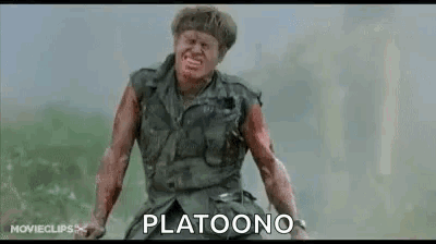 A Man In A Military Uniform Is Standing In A Field With A Bloody Face And The Words Platoono Written On The Screen . GIF