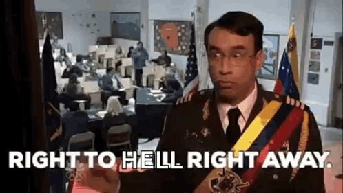 A Man In A Military Uniform Is Standing In Front Of A Room With People Sitting At Desks And Flags . GIF