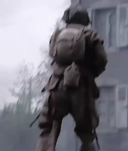 A Man In A Military Uniform Is Walking In Front Of A Building With A Backpack On His Back . GIF