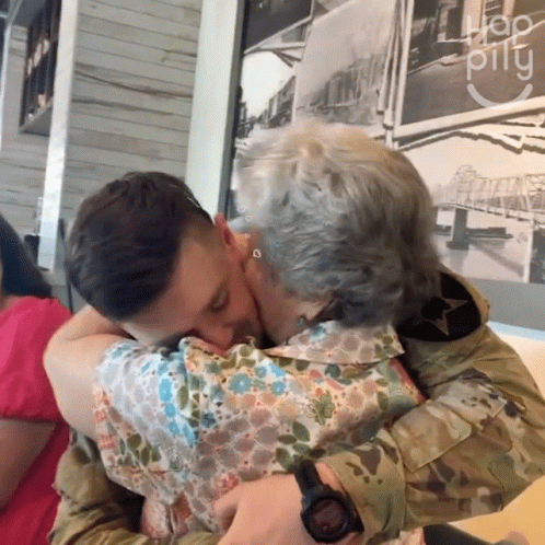 A Man In A Military Uniform Kisses A Woman In Front Of A Sign That Says " Hop Pillu " GIF