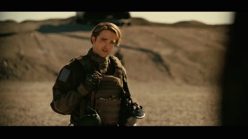 A Man In A Military Uniform Stands In A Desert Holding A Helmet GIF