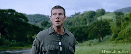 A Man In A Military Uniform Stands In A Field With Trees In The Background And A #Fantasyislandmovie Hashtag GIF