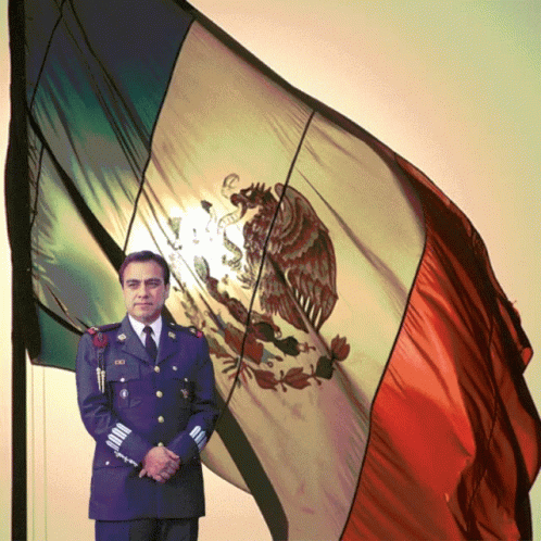 A Man In A Military Uniform Stands In Front Of A Mexican Flag With An Eagle On It GIF