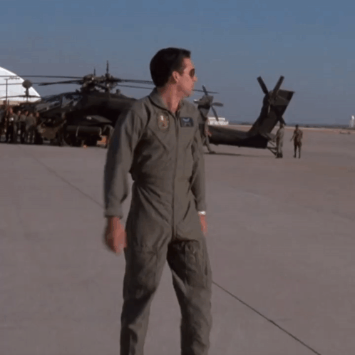 A Man In A Military Uniform Stands On A Runway In Front Of A Black Helicopter GIF