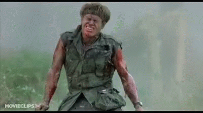 A Man In A Military Uniform With Blood On His Face And Arms Is Standing In A Field . GIF