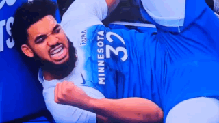 A Man In A Minnesota Jersey Is Laying On The Floor With His Fist In The Air . GIF