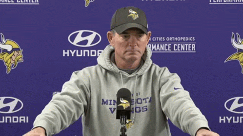 A Man In A Minnesota Vikings Hoodie Stands In Front Of A Hyundai Banner GIF