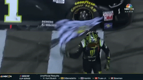 A Man In A Monster Shirt Stands In Front Of A Car That Says Good Year GIF