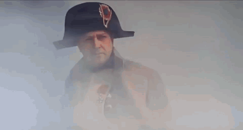 A Man In A Napoleon Hat And Coat Is Standing In Front Of A Building . GIF