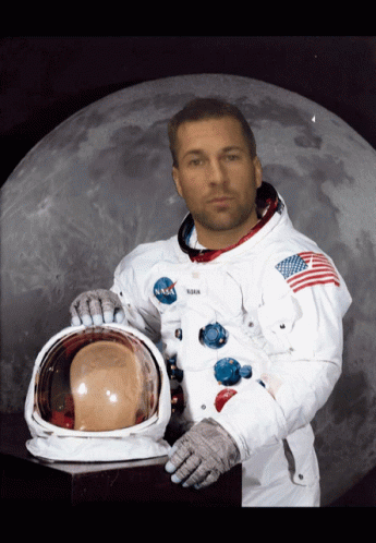 A Man In A Nasa Space Suit Holds His Helmet In Front Of A Full Moon GIF