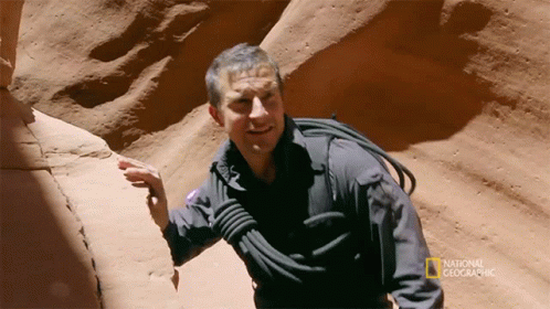 A Man In A National Geographic Shirt Is Standing In A Canyon GIF