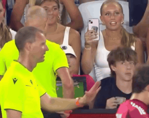 A Man In A Neon Green Shirt Is Talking To Another Man In A Crowd GIF