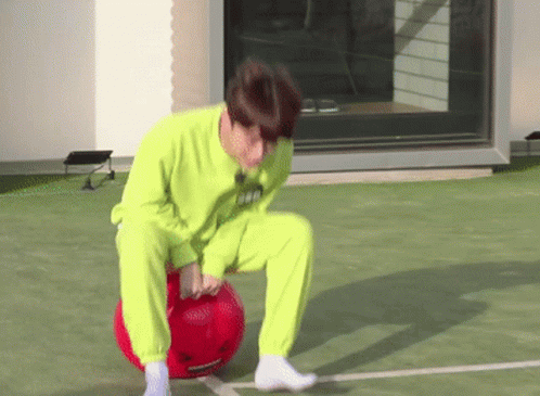 A Man In A Neon Green Sweater Is Kneeling On A Red Ball . GIF