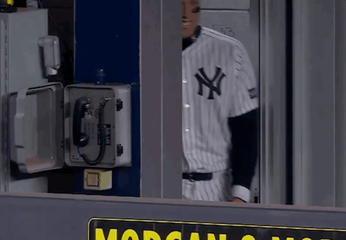 a man in a new york yankees uniform stands in front of a phone box