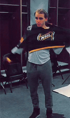 A Man In A Nhl Jersey Is Standing In A Room GIF