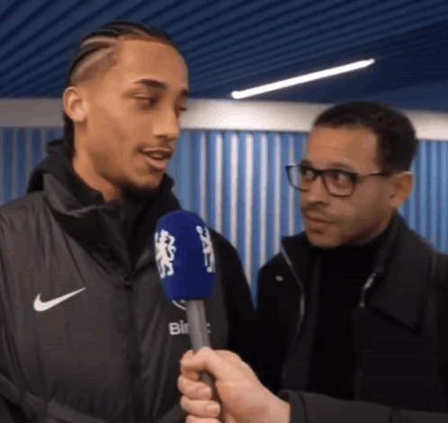 A Man In A Nike Jacket Is Being Interviewed By A Man In Glasses GIF