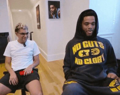 a man in a no guts no glory hoodie sits next to another man
