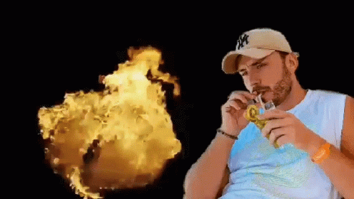 A Man In A Ny Hat Is Drinking Through A Straw In Front Of A Fireball . GIF