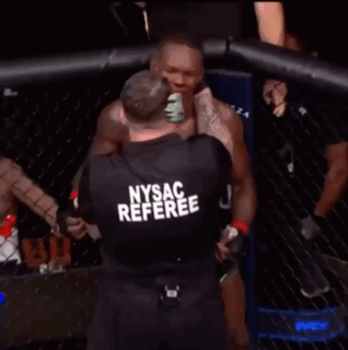A Man In A Nysac Referee Shirt Stands In Front Of A Cage GIF